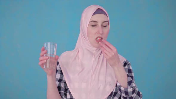 Young Beautiful Muslim Woman with a Pill and a Glass of Water Taking a Pill