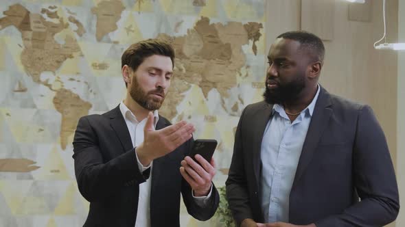 Two Employees in Business Suits are Watching a Business Application on Their Phone