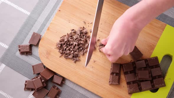 Woman Chopping Black Dark Chocolate on Wooden Cutting Board