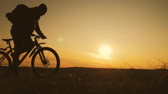 The Silhouette of the Mountain Bicycle Rider on the Hill with Bike at Sunset. Sport, Travel and