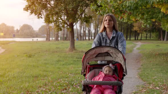 A Young Mother with a Stroller Walks in the Autumn Evening