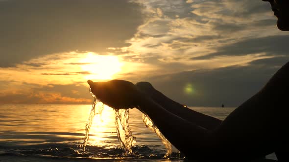 Female Hands With Water In The Sea At Sunset. Slow Motion.