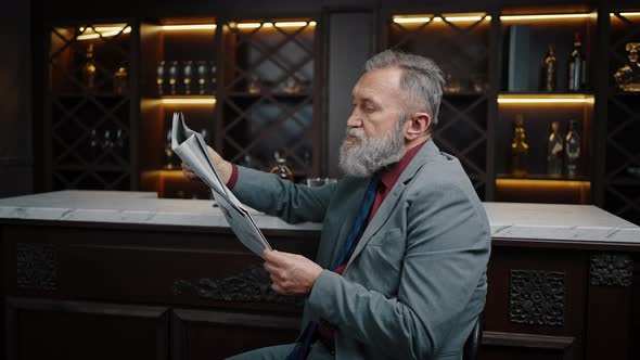 Successful Senior Businessman Reading Newspaper Sitting Alone at Bar Counter in Evening Free Space