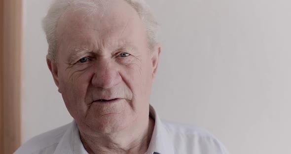 Close Portrait of Senior Man with Bright Eyes Rejoicing at Camera on Background