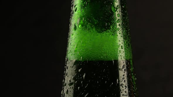 Drop of condensation drips on beer bottle glass. Water drops falling down