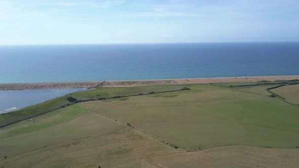 Wide aerial tracking forward over a field at the west side of Chesil Beach, Dorset. England. Bird of