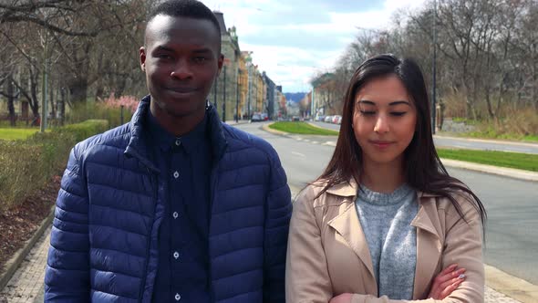 A Young Black Man and a Young Asian Woman Nod at the Camera in a Street in an Urban Area