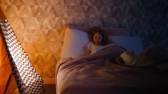 Little Girl Sleeps Tight on Bed By Children Teepee at Home