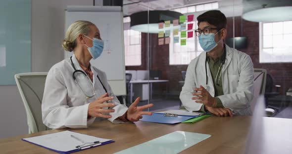 Diverse male and female doctors wearing face masks brainstorming in meeting room