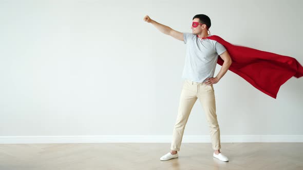 Portrait of Super Hero in Fluttering Red Cape and Mask Standing with Raised Arm