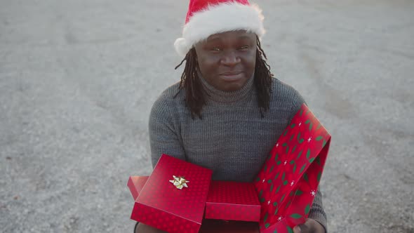 Black Man with Santa Hat Holding Bunch of Red Wrapped Christmas Presents