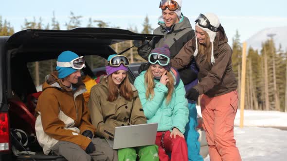 Group of young snowboarders on the slopes using laptop