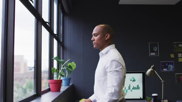 Mixed race businessman standing looking out of window in modern office