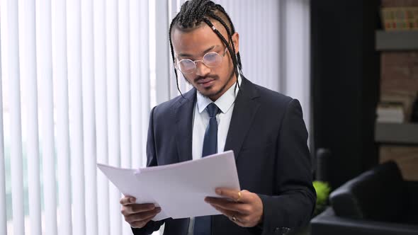 A young black man studies documents and looks up at the camera with a smile