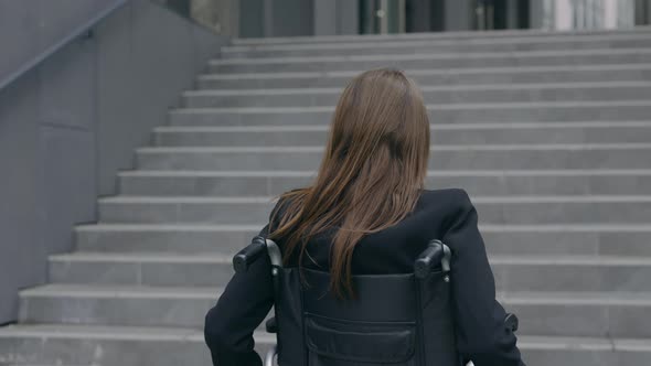 Backside View of Female Person in Suit Pushing Herself on Wheel Chair at Street