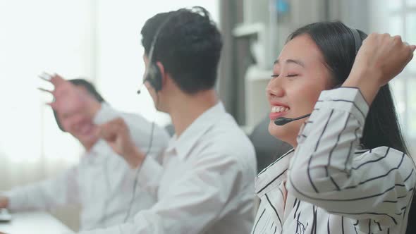 Three Asian Call Centre Agents Wearing Headsets Being Happy Due To Success Working With Computers