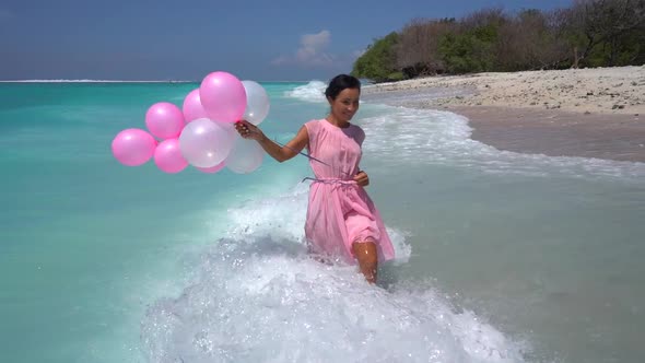 Cute Happy Woman in Pink with Balloons Walking in the Splashing Ocean Water Birthday Party on the
