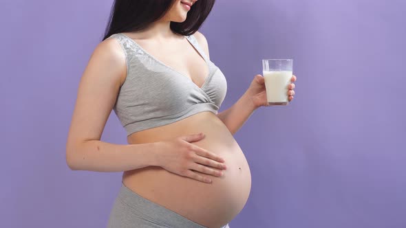 Young Pregnant Caucasian Model with Long Black Hair Holds a Glass of Milk