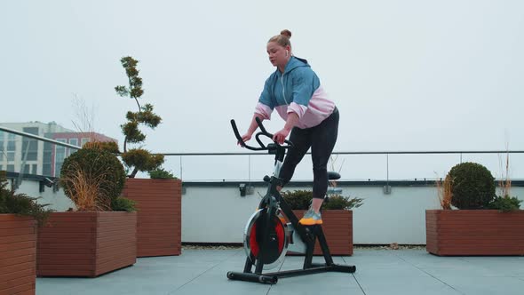 Healthy Caucasian Woman Exercising Workout on Stationary Cycling Machine Bike on House Rooftop Gym