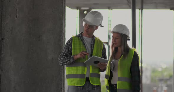 Two Engineers a Man and a Woman with a Tablet Computer at a Construction Site Condemn the