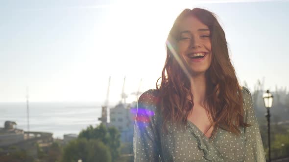 Portrait of Cheerful Woman 20s with Curly Brown Hair Wearing Dress Laughing While Walking on Sunny