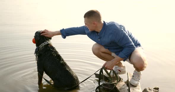 Young Man Playing with Dog Standing on Lake