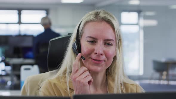 Woman wearing headset talking while sitting on her desk at office