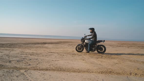 Motorcyclist Driving His Customized Fast Motorbike on the Dirt Road in Desert Around Sea or Lake