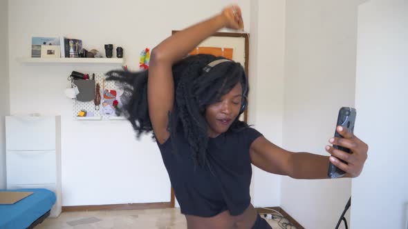 Young woman dancing and using smartphone at home