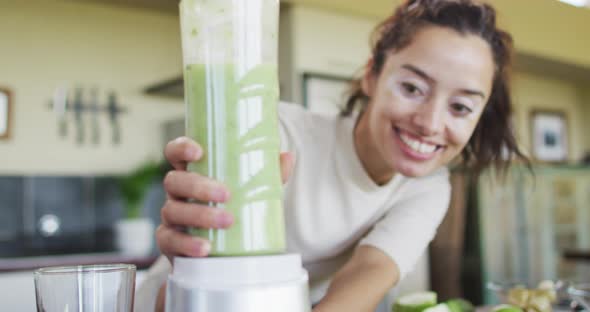 Happy biracial woman using blender, preparing smoothie in kitchen