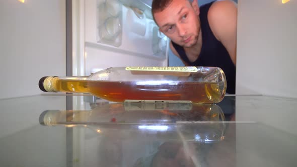 man looks into an empty refrigerator and takes out bottle of alcohol. Alcoholism