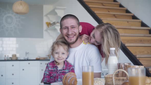 Happy Young Family Posing in Kitchen at Home. Portrait of Smiling Young Brunette Man, Blond Woman