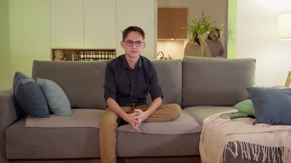 A Guy with Glasses Watches TV on the Sofa in the Evening in the Living Room