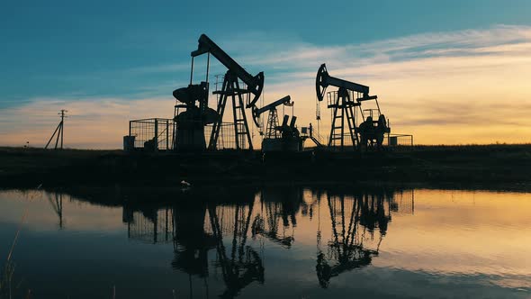 Oil Pumping Units Operating at Sunset Reflected on Water Surface