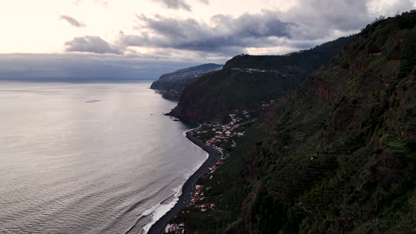 Sunset aerial along rugged Madeira coastline, small coastal village