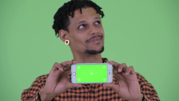 Face of Happy Young Handsome African Man Thinking While Showing Phone