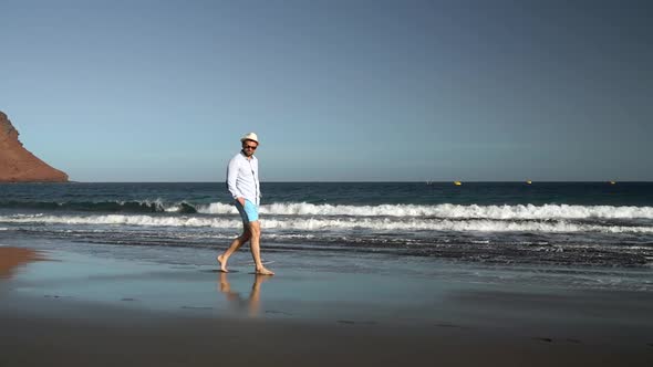 Happy Man Walking Along the Ocean Beach at Sunset