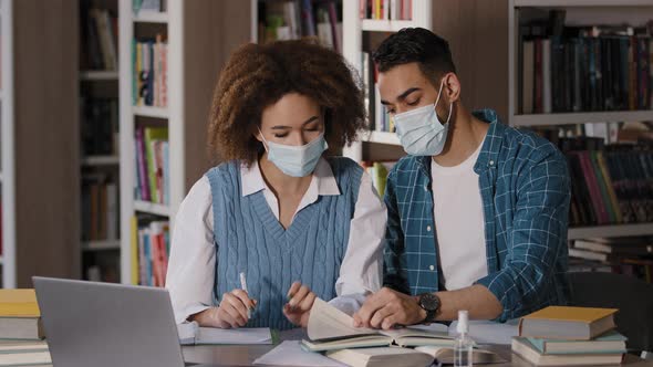 Two Students Girl and Guy in Protective Masks Sitting at Desk Listening to Online Lecture From