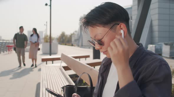 Short-Haired Asian Woman Scrolling on Smartphone Outdoors