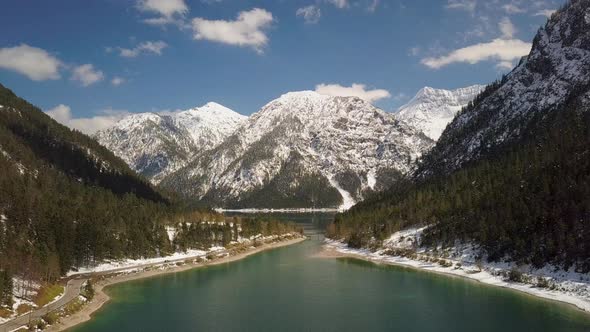 Perfect snow covered forest banks around Plansee lake aerial view towards Austria mountains landscap