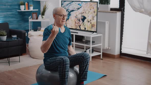 Senior Man Lifting Dumbbells and Sitting on Fitness Toning Ball