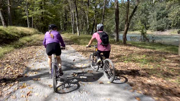 Mother and teenage son biking side by side on a rural gravel road with a river to their right side.