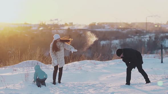 Active Family Throws White Snow Against Roofs at Sunset