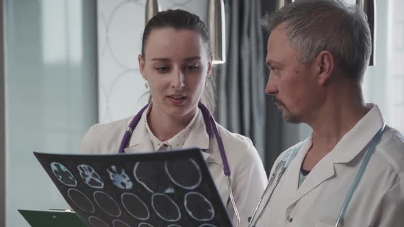 Male and Female Doctors Working Together Looking at MRI Image Standing in Hospital.