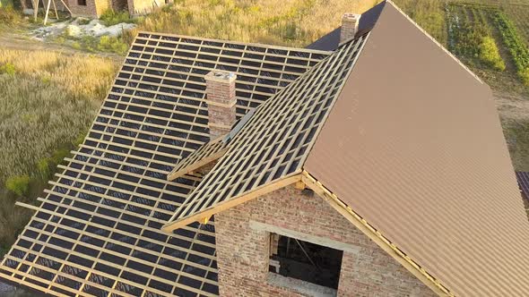 Aerial view of unfinished house with wooden roof structure covered with metal tile sheets under 