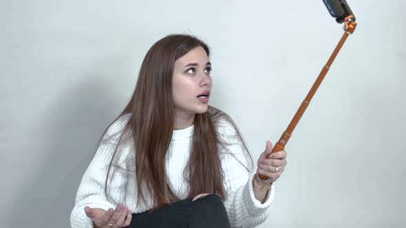 Caucasian Girl Sitting on Floor. Holds Cellphone, Waves His Hands, Says