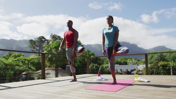 Relaxed biracial couple on terrace, practicing yoga together on mats