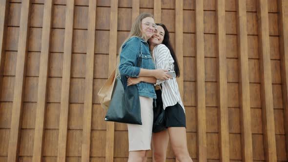 Happy Young Women Meeting Outdoors Hugging Talking Discussing Purchases in Shopping Bags