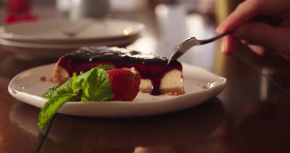 Cheesecake on a White Plate Drizzled with Blueberry Jam on Top Garnished with Strawberries and Mint