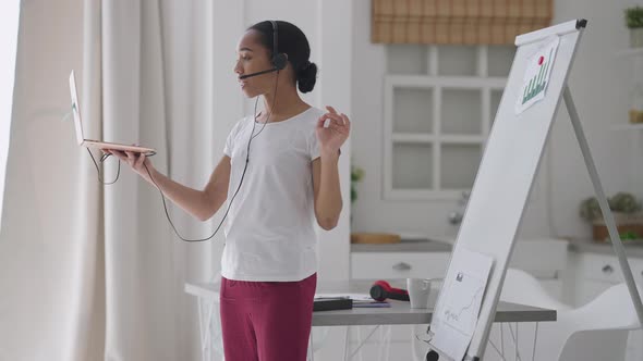 Confident Slim Beautiful Woman in Headphones Pointing at Business Graphs on Whiteboard Talking at